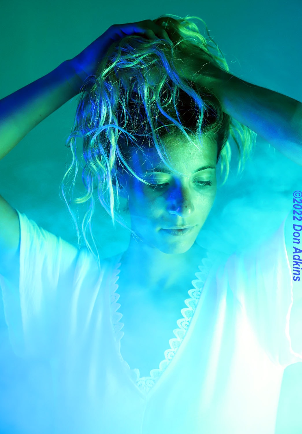 Fine art portrait with cyan and teal neon lighting, hands in hair